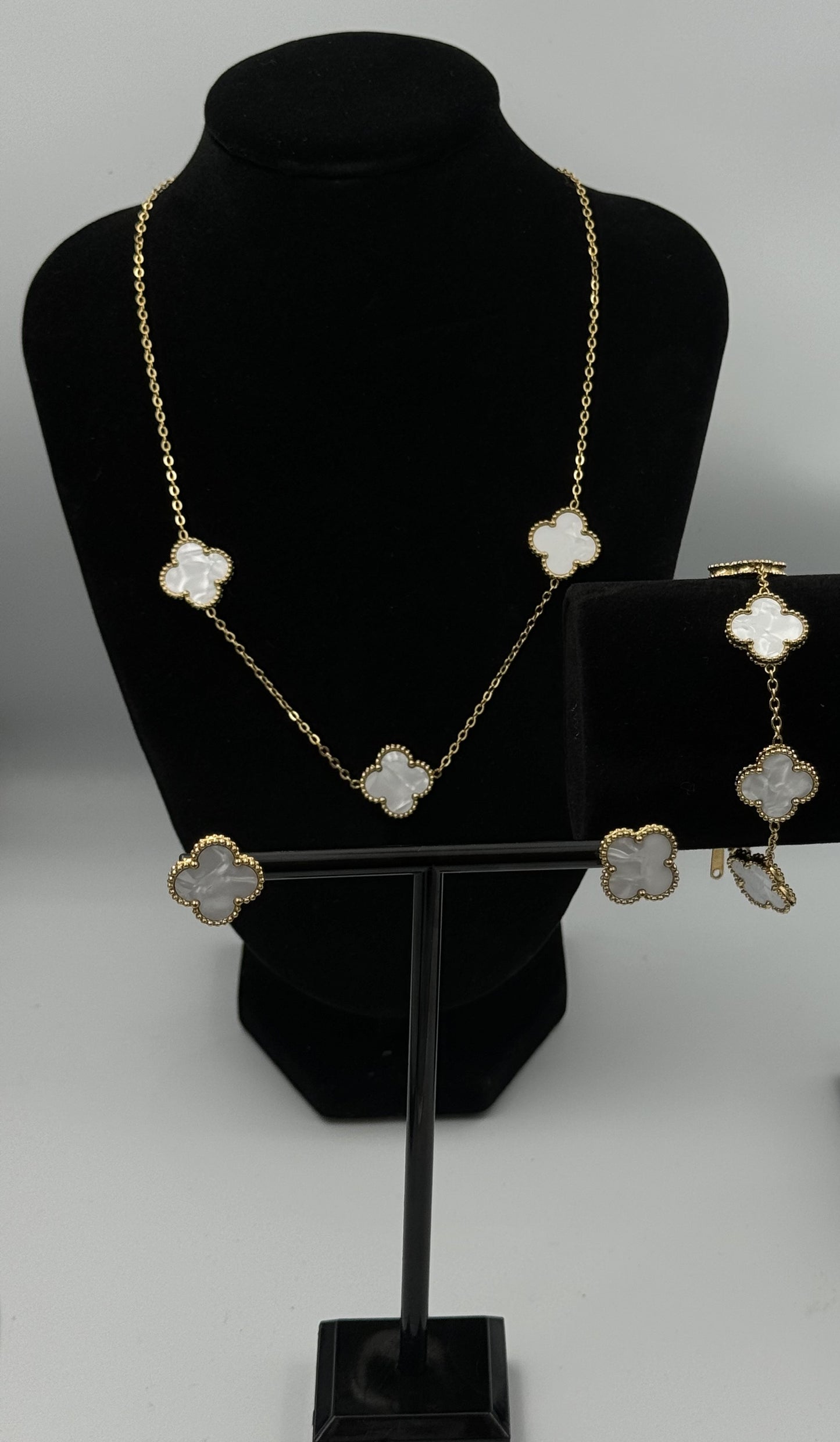 “Mizori Jewelry white and gold stainless steel clover jewelry set on stand, including bracelet, necklace, and earrings, elegant minimalist design